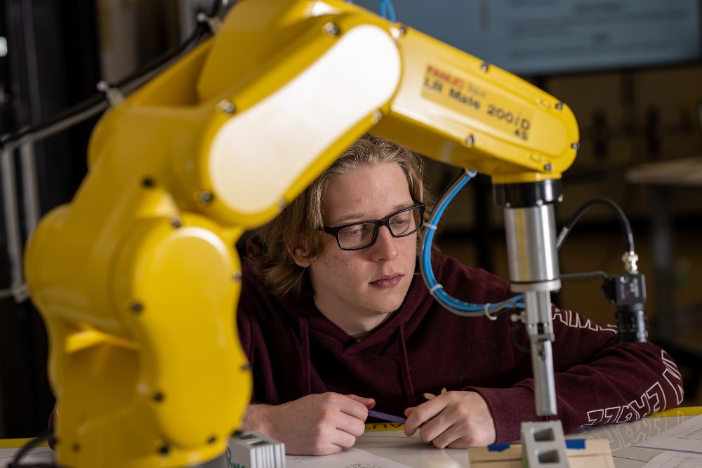 A student programming a yellow FANUC robotic arm in the engineering technology lab.