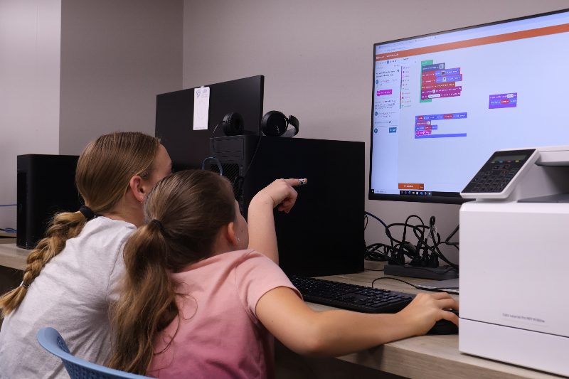 Two campers pointing at a block-coding project on a monitor in the Workforce Center computer lab.