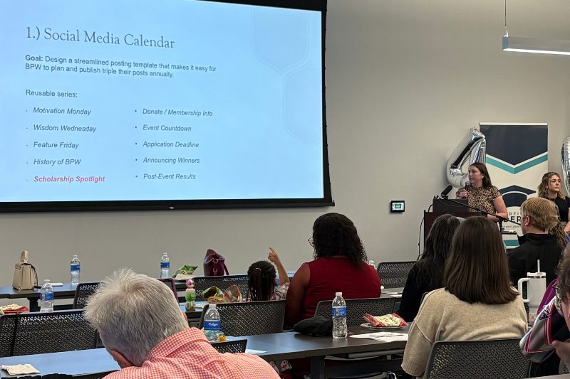 An audience watching a presentation on the large screen in the conference room.