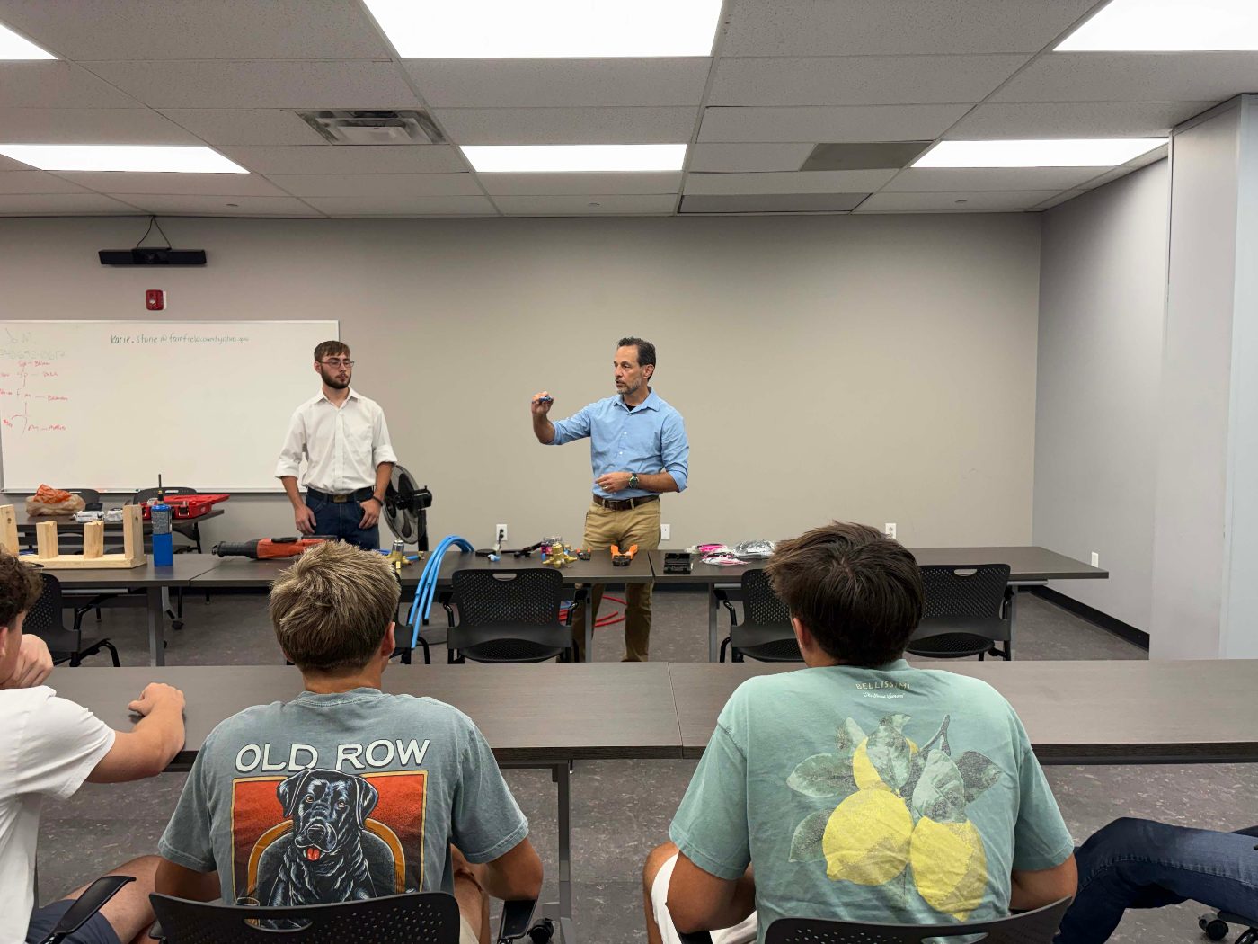 Plumbing instructors showing tools and fittings to students in the classroom.