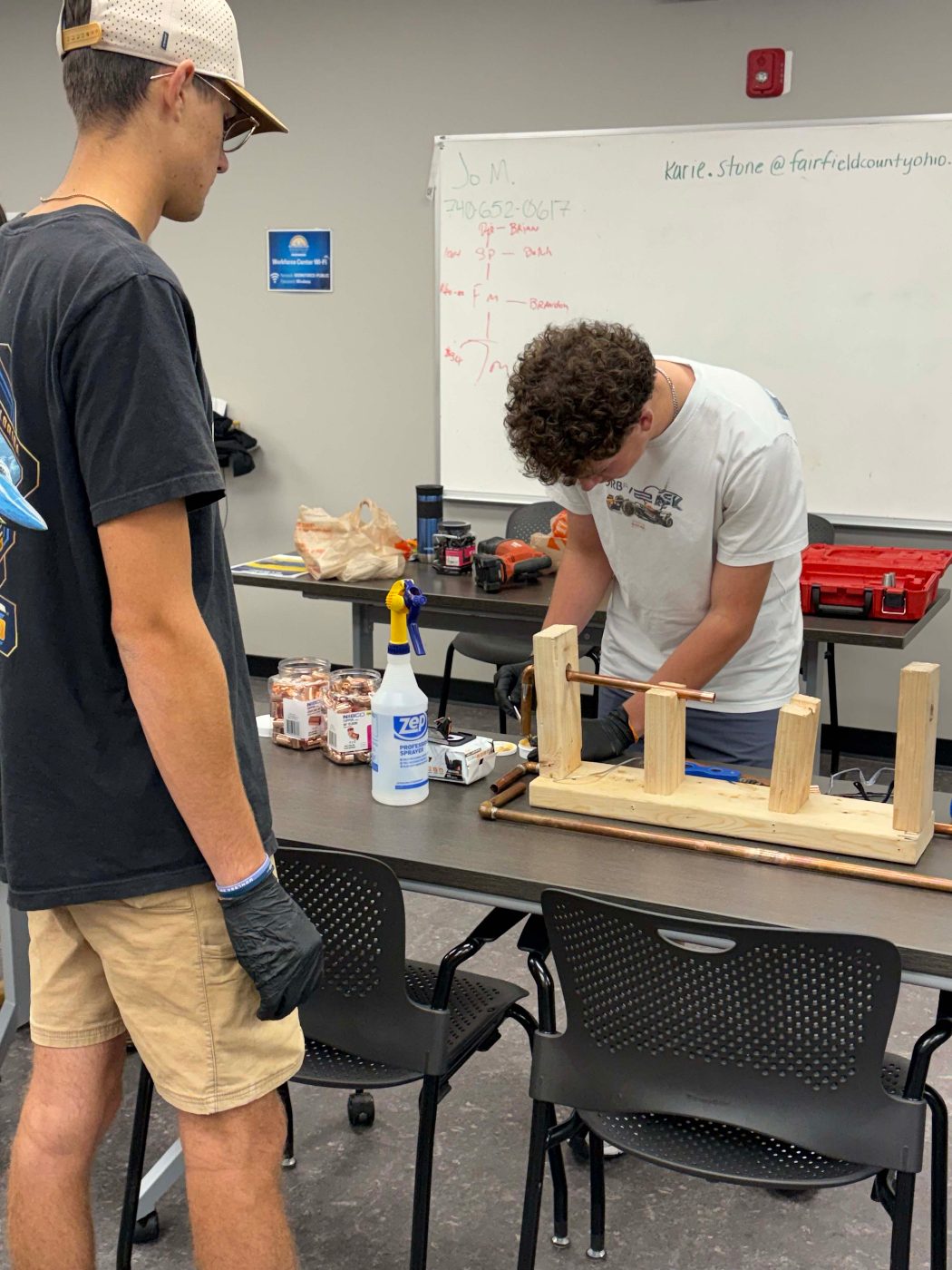 A student working on copper pipe in a wooden practice stand.