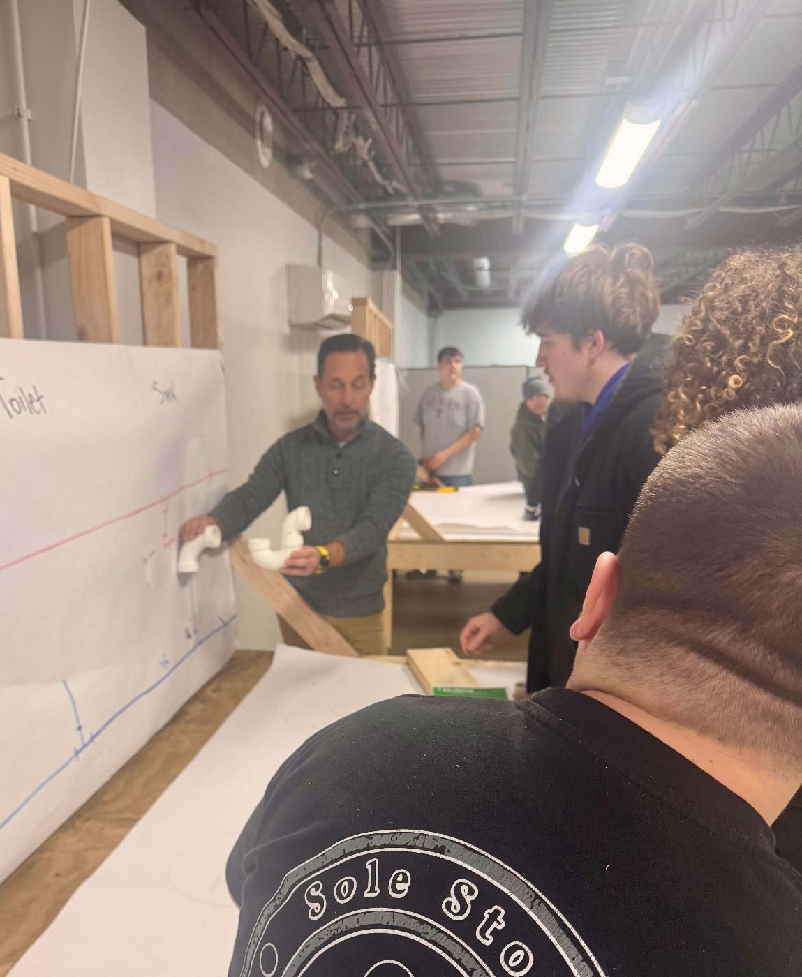 A Freeland Plumbing instructor showing students how drain fittings fit a wall layout.