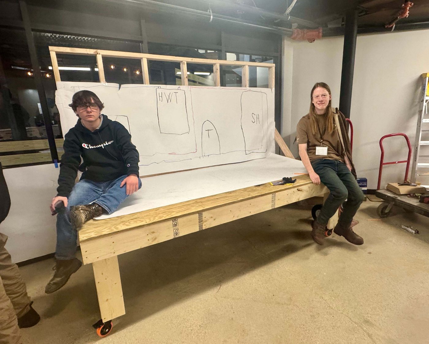 Two plumbing students sitting on the residential plumbing mock-up frame they are building.